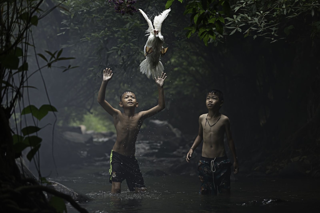 Photo and caption by sarah woutersTwo boys are trying to catch a duck at the stream of the waterfall. Nong Khai Province, Thailand.